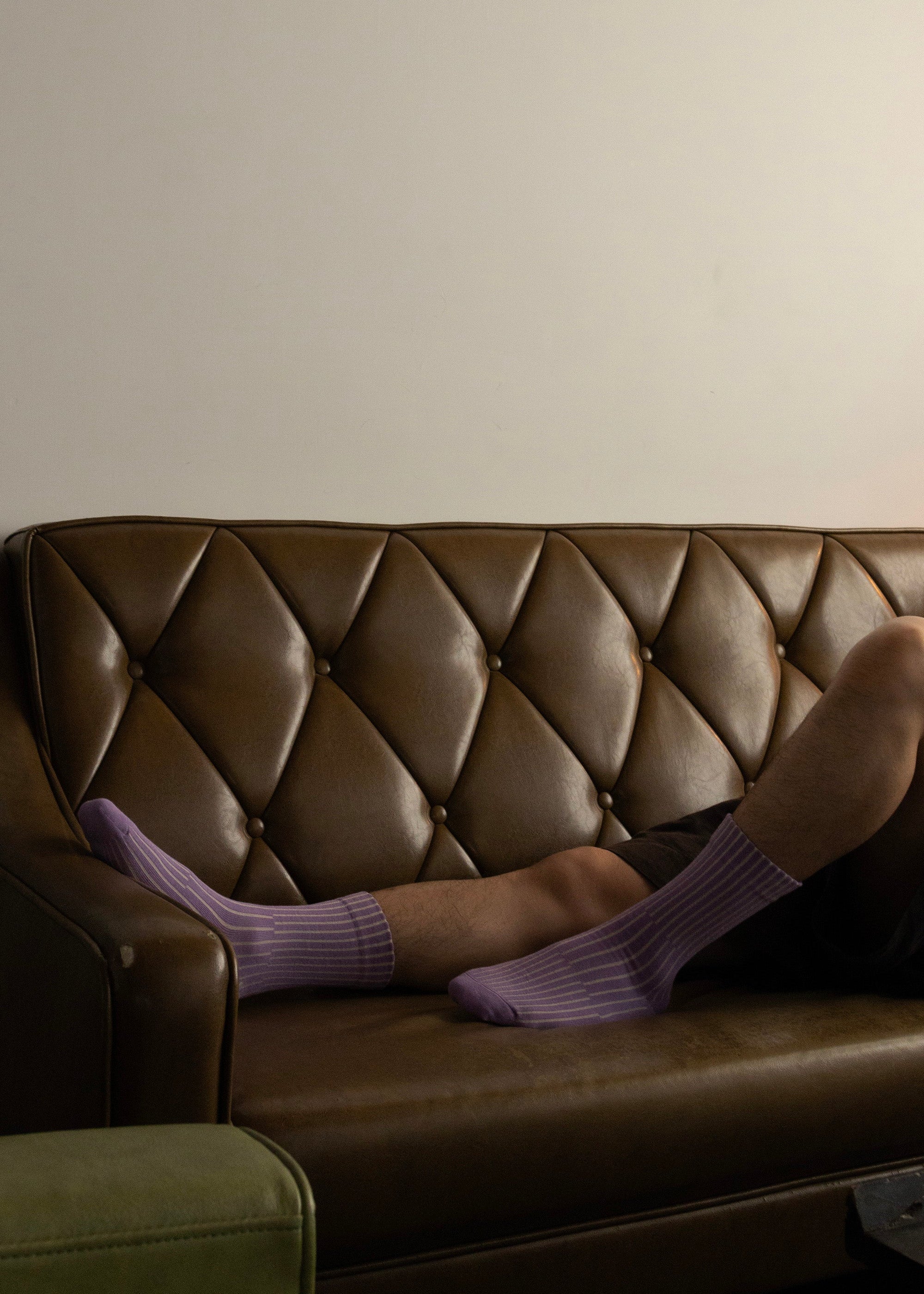Person wearing the lilac split socks laying on a brown leather couch against a beige wall.
