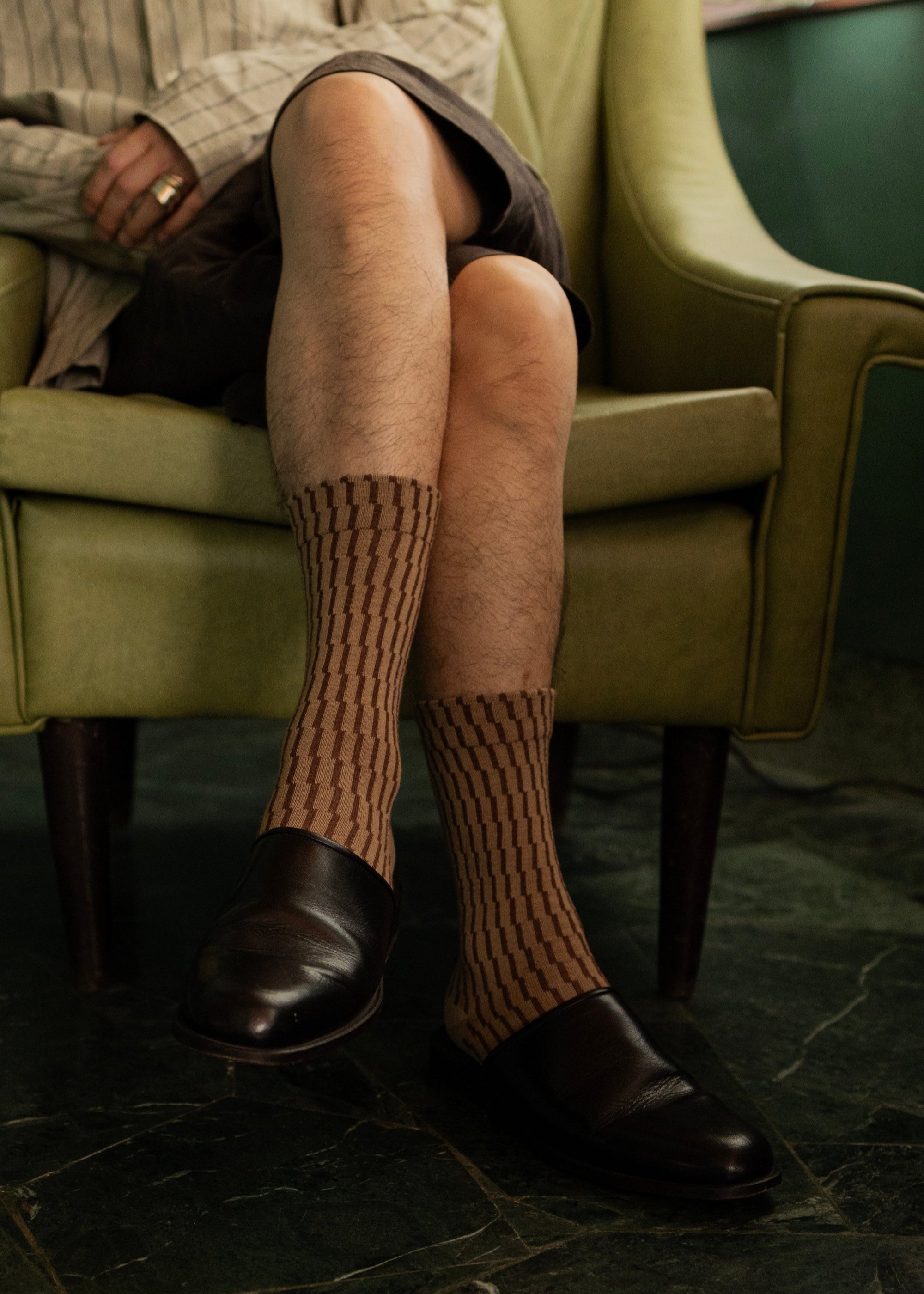 Person wearing wool shifting grid socks and loafer sitting on a green couch.