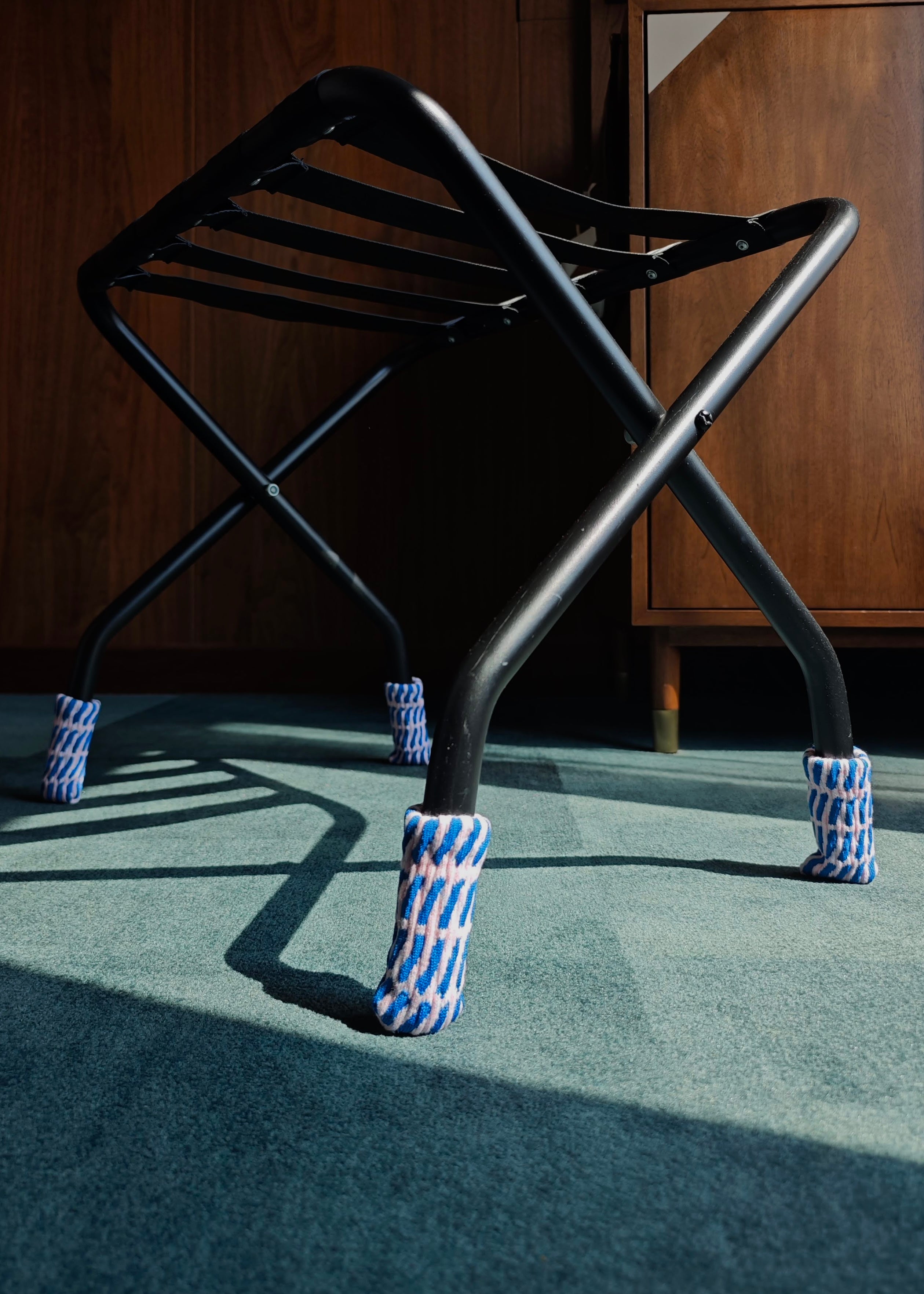 Black metal stool with blue and pink chair leg cover on a green carpet