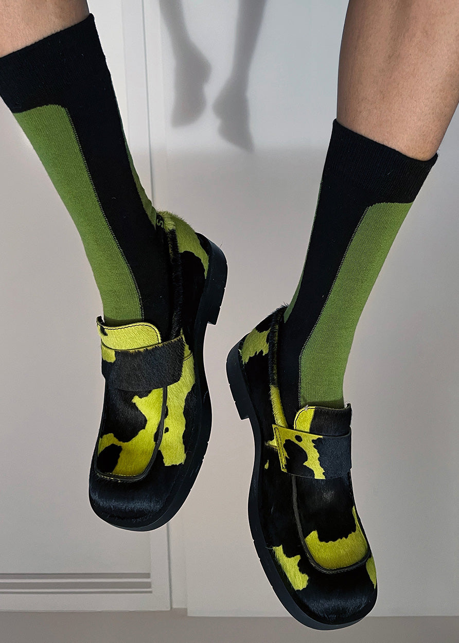 A closer up of a person wearing a acid color hide loafer with the Fence cotton socks in color Black and Grass