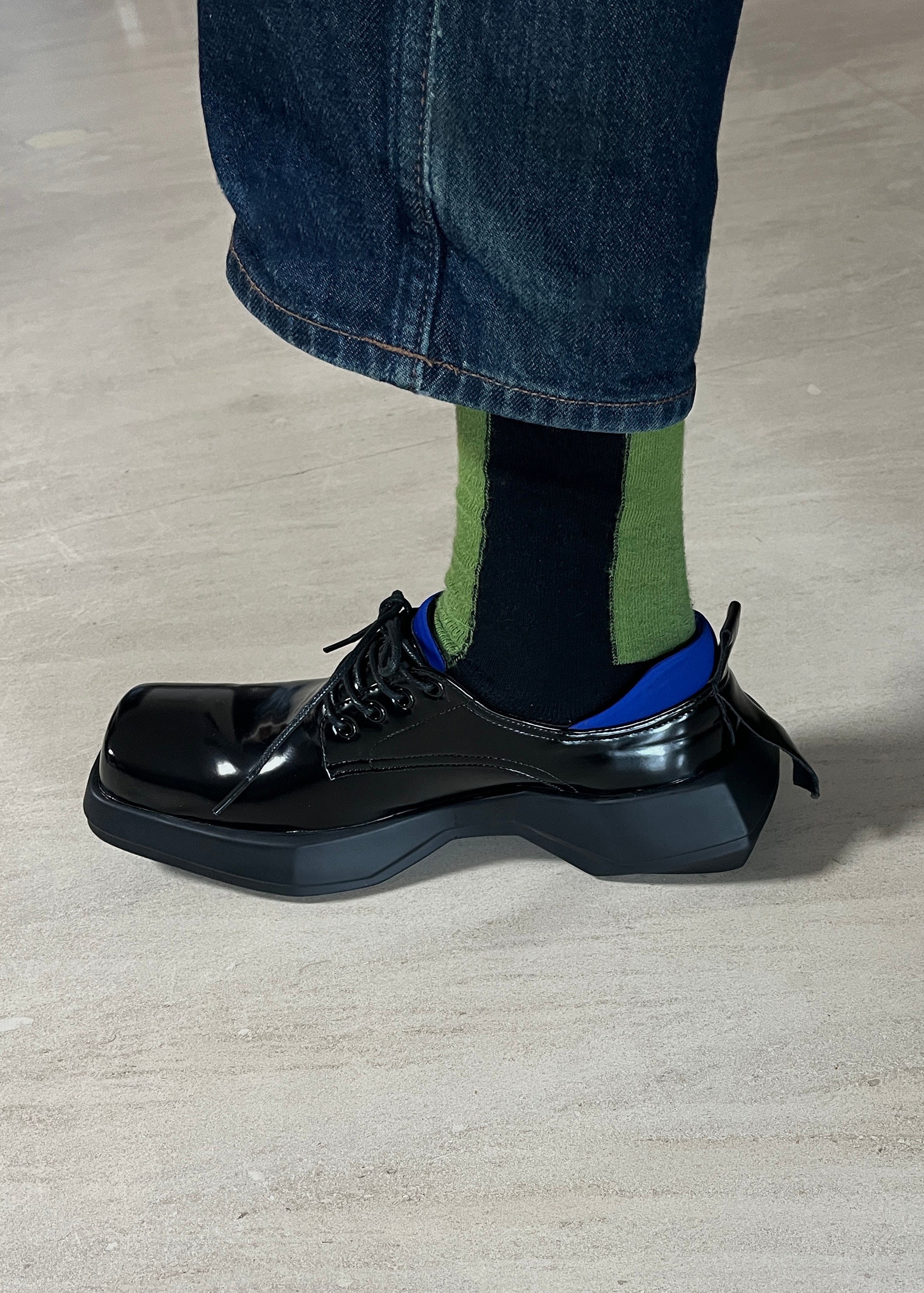 Close up on a person wearing a black leather loafer with The Fence Cotton Dress Socks in Color Black and Grass