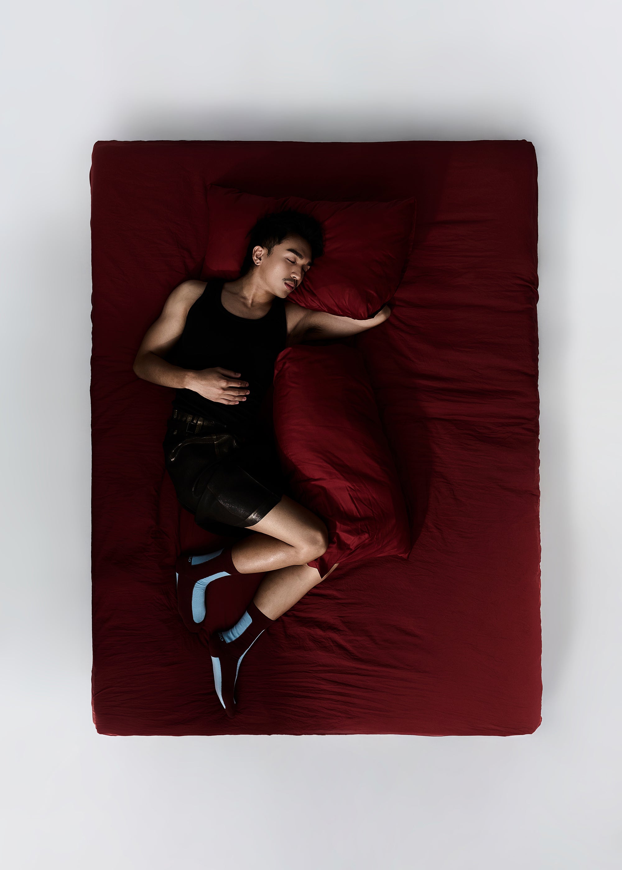 Person lying on a Burgundy Bed wearing the Fence Cotton Dress Socks in Color Maroon and Sky