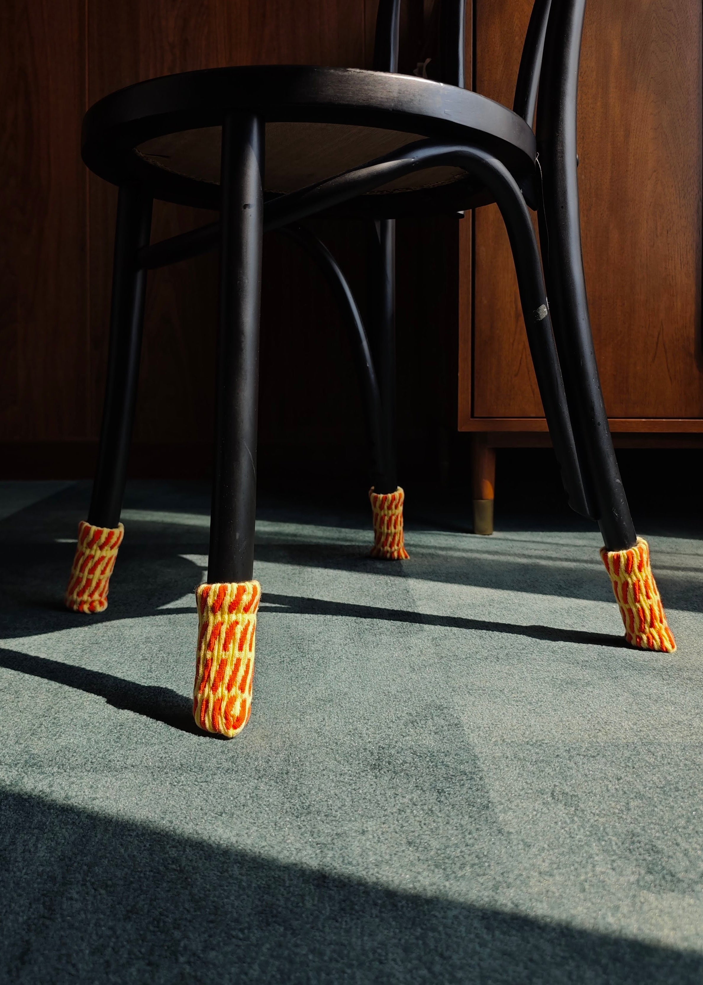 Black chair with orange foot protectors on a gray floor.