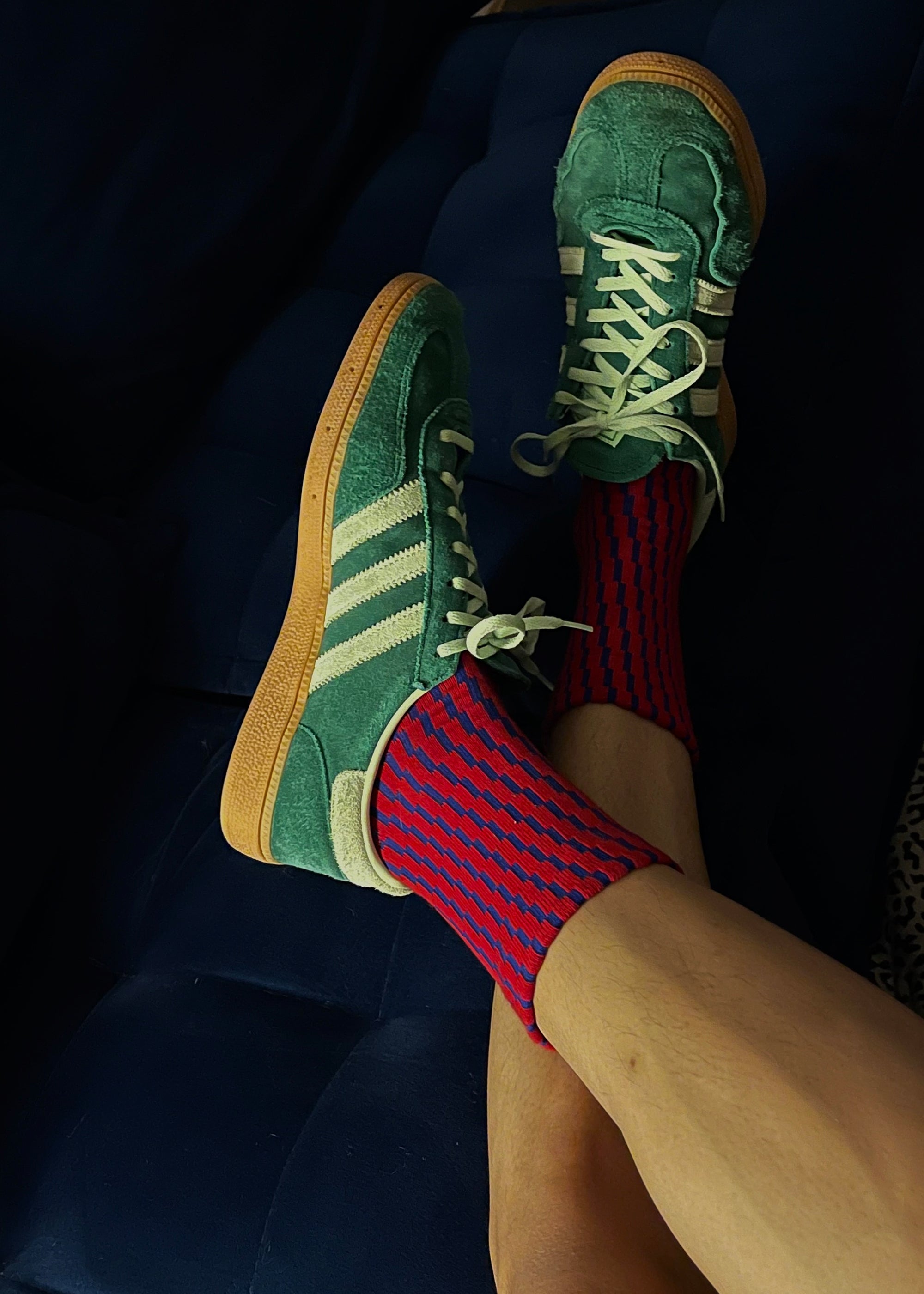 Close up of a person wearing a green adidas sneaker with the Shifting Grid Rib Socks in Color Red and Ultramarine