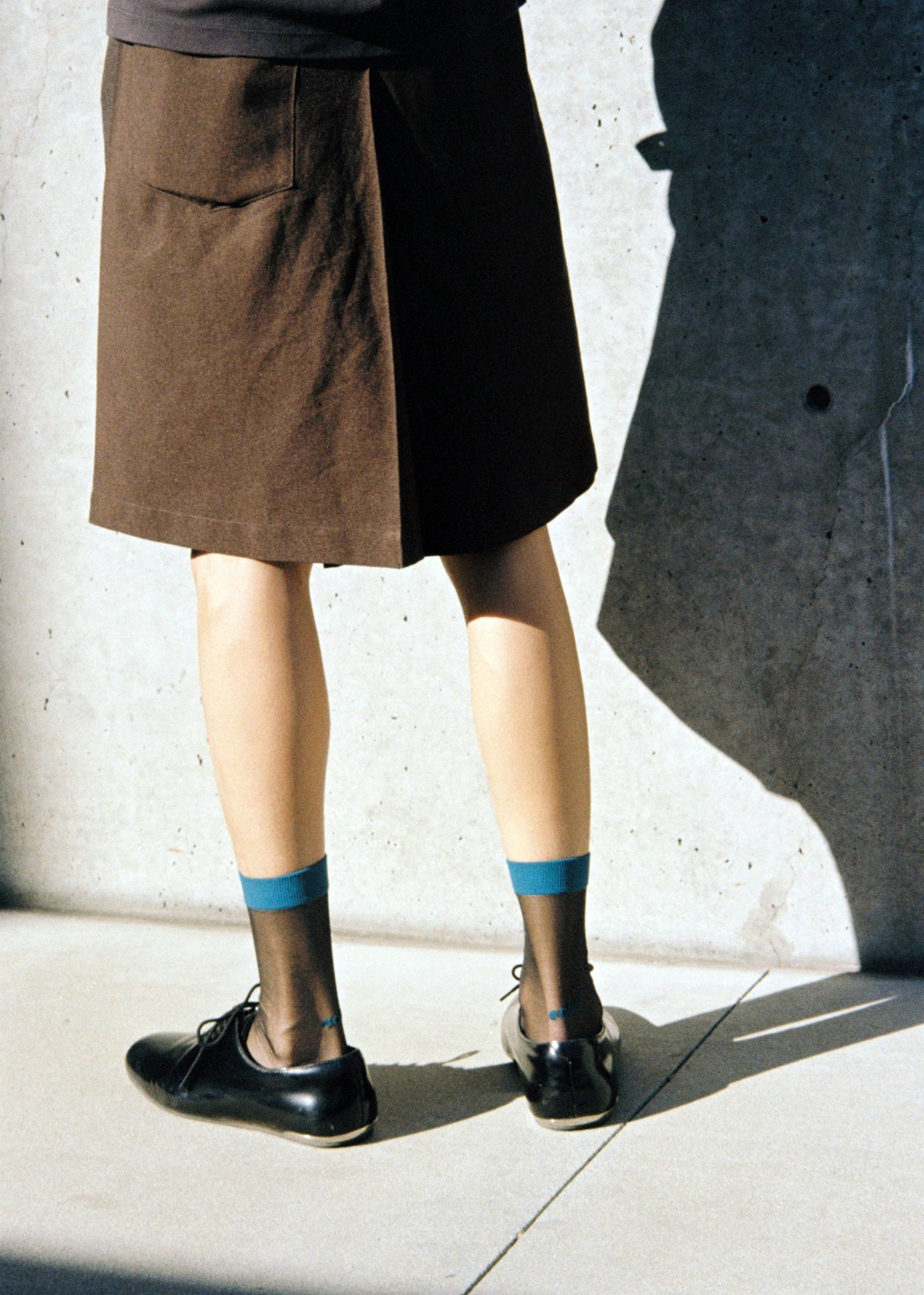 Person wearing a brown skirt, black loafer with The Suit Sheer Socks in Color Cyan Night. 