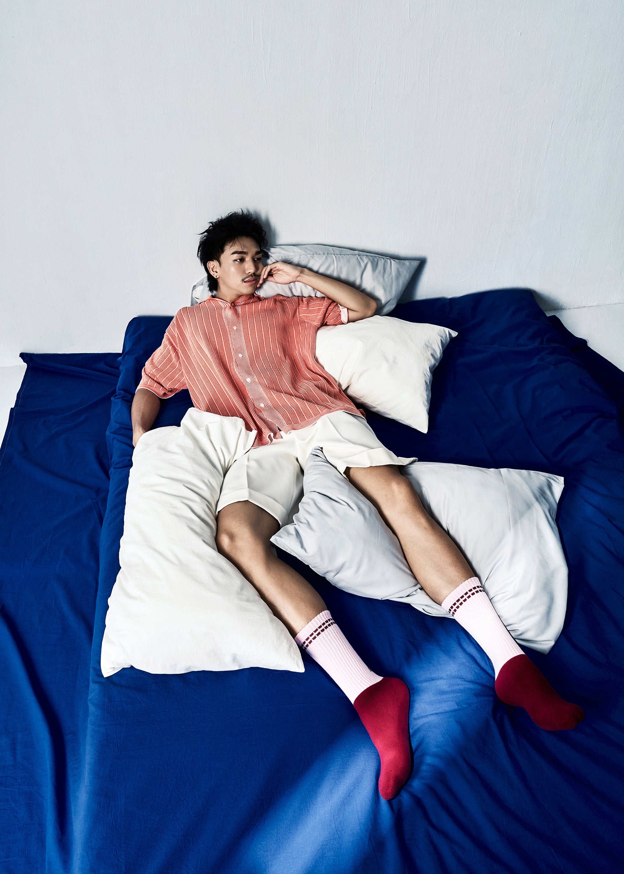Model lying on a bed wearing a red knitted shirt and white shorts with the Track Cotton Athletic Socks in Color Azure